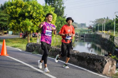 Jogja Maratonu 42K 'nın katılımcıları veya koşucuları, Prambanan tapınak köyünün etrafından güzel bir yoldan geçiyorlar. : Yogyakarta, Endonezya - 18 Haziran 2023