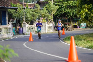 Jogja Maratonu 42K 'nın katılımcıları veya koşucuları, Prambanan tapınak köyünün etrafından güzel bir yoldan geçiyorlar. : Yogyakarta, Endonezya - 18 Haziran 2023