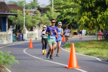 Jogja Maratonu 42K 'nın katılımcıları veya koşucuları, Prambanan tapınak köyünün etrafından güzel bir yoldan geçiyorlar. : Yogyakarta, Endonezya - 18 Haziran 2023