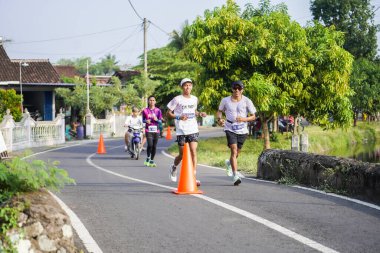 Jogja Maratonu 42K 'nın katılımcıları veya koşucuları, Prambanan tapınak köyünün etrafından güzel bir yoldan geçiyorlar. : Yogyakarta, Endonezya - 18 Haziran 2023
