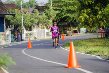 Jogja Maratonu 42K 'nın katılımcıları veya koşucuları, Prambanan tapınak köyünün etrafından güzel bir yoldan geçiyorlar. : Yogyakarta, Endonezya - 18 Haziran 2023