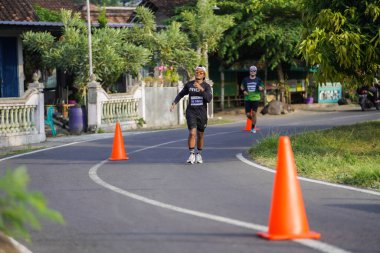 Jogja Maratonu 42K 'nın katılımcıları veya koşucuları, Prambanan tapınak köyünün etrafından güzel bir yoldan geçiyorlar. : Yogyakarta, Endonezya - 18 Haziran 2023