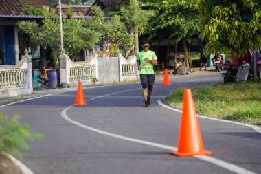 Jogja Maratonu 42K 'nın katılımcıları veya koşucuları, Prambanan tapınak köyünün etrafından güzel bir yoldan geçiyorlar. : Yogyakarta, Endonezya - 18 Haziran 2023
