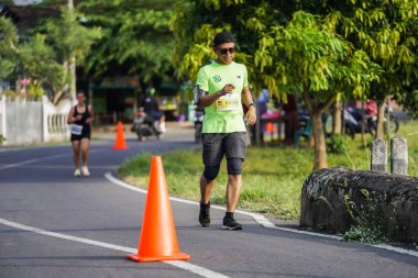 Jogja Maratonu 42K 'nın katılımcıları veya koşucuları, Prambanan tapınak köyünün etrafından güzel bir yoldan geçiyorlar. : Yogyakarta, Endonezya - 18 Haziran 2023