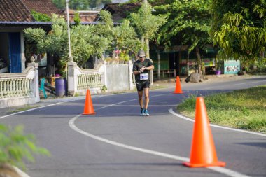Jogja Maratonu 42K 'nın katılımcıları veya koşucuları, Prambanan tapınak köyünün etrafından güzel bir yoldan geçiyorlar. : Yogyakarta, Endonezya - 18 Haziran 2023