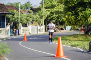 Jogja Maratonu 42K 'nın katılımcıları veya koşucuları, Prambanan tapınak köyünün etrafından güzel bir yoldan geçiyorlar. : Yogyakarta, Endonezya - 18 Haziran 2023
