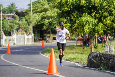 Jogja Maratonu 42K 'nın katılımcıları veya koşucuları, Prambanan tapınak köyünün etrafından güzel bir yoldan geçiyorlar. : Yogyakarta, Endonezya - 18 Haziran 2023