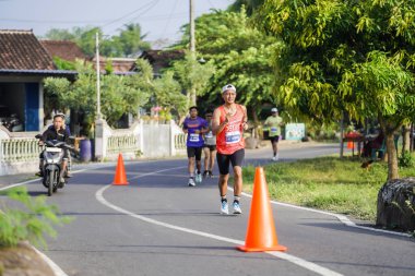Jogja Maratonu 42K 'nın katılımcıları veya koşucuları, Prambanan tapınak köyünün etrafından güzel bir yoldan geçiyorlar. : Yogyakarta, Endonezya - 18 Haziran 2023