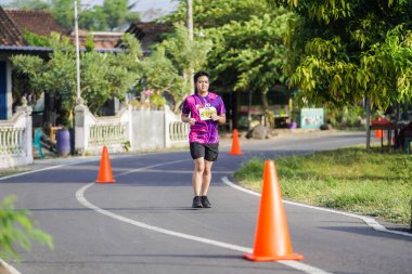 Jogja Maratonu 42K 'nın katılımcıları veya koşucuları, Prambanan tapınak köyünün etrafından güzel bir yoldan geçiyorlar. : Yogyakarta, Endonezya - 18 Haziran 2023