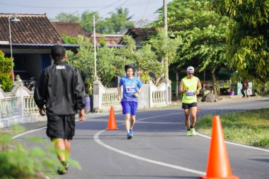 Jogja Maratonu 42K 'nın katılımcıları veya koşucuları, Prambanan tapınak köyünün etrafından güzel bir yoldan geçiyorlar. : Yogyakarta, Endonezya - 18 Haziran 2023