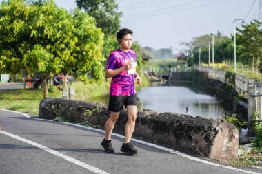 Jogja Maratonu 42K 'nın katılımcıları veya koşucuları, Prambanan tapınak köyünün etrafından güzel bir yoldan geçiyorlar. : Yogyakarta, Endonezya - 18 Haziran 2023