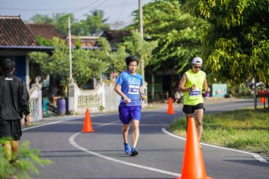 Jogja Maratonu 42K 'nın katılımcıları veya koşucuları, Prambanan tapınak köyünün etrafından güzel bir yoldan geçiyorlar. : Yogyakarta, Endonezya - 18 Haziran 2023