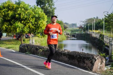 Jogja Maratonu 42K 'nın katılımcıları veya koşucuları, Prambanan tapınak köyünün etrafından güzel bir yoldan geçiyorlar. : Yogyakarta, Endonezya - 18 Haziran 2023