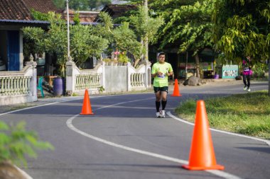 Jogja Maratonu 42K 'nın katılımcıları veya koşucuları, Prambanan tapınak köyünün etrafından güzel bir yoldan geçiyorlar. : Yogyakarta, Endonezya - 18 Haziran 2023