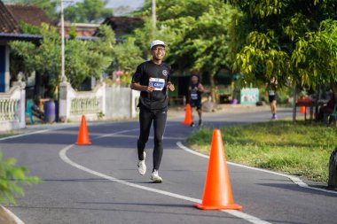 Jogja Maratonu 42K 'nın katılımcıları veya koşucuları, Prambanan tapınak köyünün etrafından güzel bir yoldan geçiyorlar. : Yogyakarta, Endonezya - 18 Haziran 2023