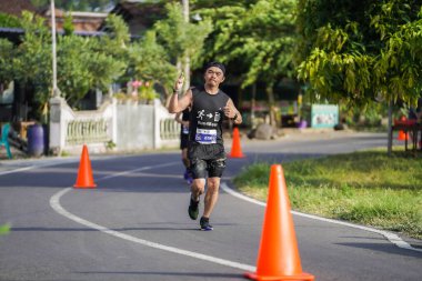 Jogja Maratonu 42K 'nın katılımcıları veya koşucuları, Prambanan tapınak köyünün etrafından güzel bir yoldan geçiyorlar. : Yogyakarta, Endonezya - 18 Haziran 2023