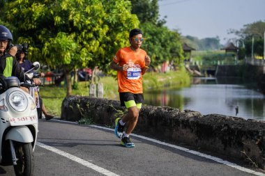 Jogja Maratonu 42K 'nın katılımcıları veya koşucuları, Prambanan tapınak köyünün etrafından güzel bir yoldan geçiyorlar. : Yogyakarta, Endonezya - 18 Haziran 2023