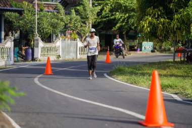 Jogja Maratonu 42K 'nın katılımcıları veya koşucuları, Prambanan tapınak köyünün etrafından güzel bir yoldan geçiyorlar. : Yogyakarta, Endonezya - 18 Haziran 2023