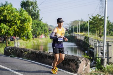 Jogja Maratonu 42K 'nın katılımcıları veya koşucuları, Prambanan tapınak köyünün etrafından güzel bir yoldan geçiyorlar. : Yogyakarta, Endonezya - 18 Haziran 2023