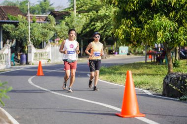 Jogja Maratonu 42K 'nın katılımcıları veya koşucuları, Prambanan tapınak köyünün etrafından güzel bir yoldan geçiyorlar. : Yogyakarta, Endonezya - 18 Haziran 2023