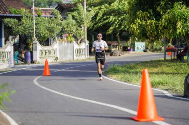 Jogja Maratonu 42K 'nın katılımcıları veya koşucuları, Prambanan tapınak köyünün etrafından güzel bir yoldan geçiyorlar. : Yogyakarta, Endonezya - 18 Haziran 2023