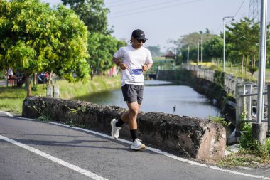 Jogja Maratonu 42K 'nın katılımcıları veya koşucuları, Prambanan tapınak köyünün etrafından güzel bir yoldan geçiyorlar. : Yogyakarta, Endonezya - 18 Haziran 2023