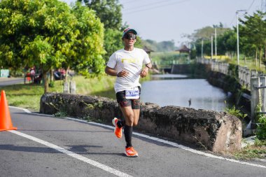 Jogja Maratonu 42K 'nın katılımcıları veya koşucuları, Prambanan tapınak köyünün etrafından güzel bir yoldan geçiyorlar. : Yogyakarta, Endonezya - 18 Haziran 2023