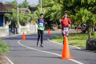 Jogja Maratonu 42K 'nın katılımcıları veya koşucuları, Prambanan tapınak köyünün etrafından güzel bir yoldan geçiyorlar. : Yogyakarta, Endonezya - 18 Haziran 2023