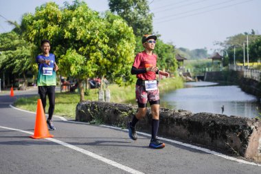 Jogja Maratonu 42K 'nın katılımcıları veya koşucuları, Prambanan tapınak köyünün etrafından güzel bir yoldan geçiyorlar. : Yogyakarta, Endonezya - 18 Haziran 2023