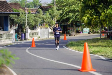 Jogja Maratonu 42K 'nın katılımcıları veya koşucuları, Prambanan tapınak köyünün etrafından güzel bir yoldan geçiyorlar. : Yogyakarta, Endonezya - 18 Haziran 2023