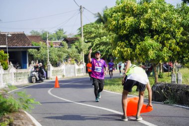 Jogja Maratonu 42K 'nın katılımcıları veya koşucuları, Prambanan tapınak köyünün etrafından güzel bir yoldan geçiyorlar. : Yogyakarta, Endonezya - 18 Haziran 2023