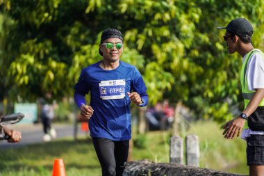 Jogja Maratonu 42K 'nın katılımcıları veya koşucuları, Prambanan tapınak köyünün etrafından güzel bir yoldan geçiyorlar. : Yogyakarta, Endonezya - 18 Haziran 2023