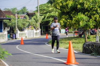Jogja Maratonu 42K 'nın katılımcıları veya koşucuları, Prambanan tapınak köyünün etrafından güzel bir yoldan geçiyorlar. : Yogyakarta, Endonezya - 18 Haziran 2023