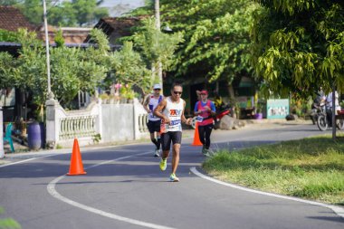 Jogja Maratonu 42K 'nın katılımcıları veya koşucuları, Prambanan tapınak köyünün etrafından güzel bir yoldan geçiyorlar. : Yogyakarta, Endonezya - 18 Haziran 2023