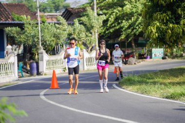 Jogja Maratonu 42K 'nın katılımcıları veya koşucuları, Prambanan tapınak köyünün etrafından güzel bir yoldan geçiyorlar. : Yogyakarta, Endonezya - 18 Haziran 2023