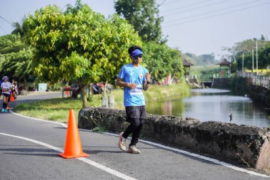 Jogja Maratonu 42K 'nın katılımcıları veya koşucuları, Prambanan tapınak köyünün etrafından güzel bir yoldan geçiyorlar. : Yogyakarta, Endonezya - 18 Haziran 2023