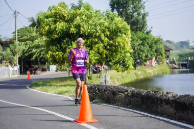 Jogja Maratonu 42K 'nın katılımcıları veya koşucuları, Prambanan tapınak köyünün etrafından güzel bir yoldan geçiyorlar. : Yogyakarta, Endonezya - 18 Haziran 2023