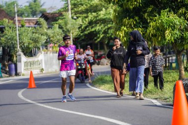 Jogja Maratonu 42K 'nın katılımcıları veya koşucuları, Prambanan tapınak köyünün etrafından güzel bir yoldan geçiyorlar. : Yogyakarta, Endonezya - 18 Haziran 2023