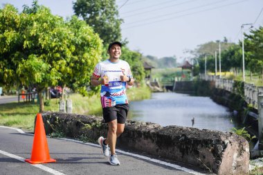 Jogja Maratonu 42K 'nın katılımcıları veya koşucuları, Prambanan tapınak köyünün etrafından güzel bir yoldan geçiyorlar. : Yogyakarta, Endonezya - 18 Haziran 2023