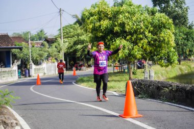 Jogja Maratonu 42K 'nın katılımcıları veya koşucuları, Prambanan tapınak köyünün etrafından güzel bir yoldan geçiyorlar. : Yogyakarta, Endonezya - 18 Haziran 2023
