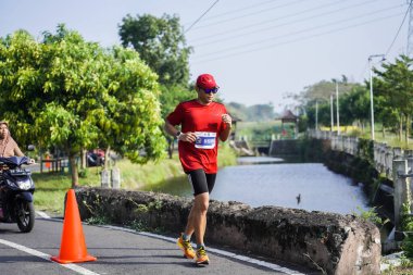 Jogja Maratonu 42K 'nın katılımcıları veya koşucuları, Prambanan tapınak köyünün etrafından güzel bir yoldan geçiyorlar. : Yogyakarta, Endonezya - 18 Haziran 2023