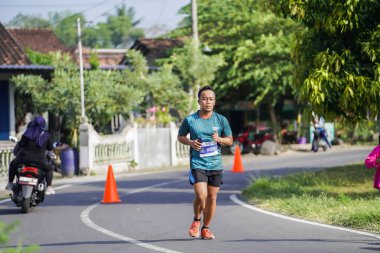 Jogja Maratonu 42K 'nın katılımcıları veya koşucuları, Prambanan tapınak köyünün etrafından güzel bir yoldan geçiyorlar. : Yogyakarta, Endonezya - 18 Haziran 2023