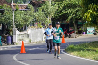 Jogja Maratonu 42K 'nın katılımcıları veya koşucuları, Prambanan tapınak köyünün etrafından güzel bir yoldan geçiyorlar. : Yogyakarta, Endonezya - 18 Haziran 2023