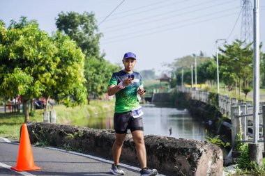 Jogja Maratonu 42K 'nın katılımcıları veya koşucuları, Prambanan tapınak köyünün etrafından güzel bir yoldan geçiyorlar. : Yogyakarta, Endonezya - 18 Haziran 2023