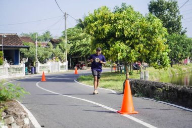 Jogja Maratonu 42K 'nın katılımcıları veya koşucuları, Prambanan tapınak köyünün etrafından güzel bir yoldan geçiyorlar. : Yogyakarta, Endonezya - 18 Haziran 2023