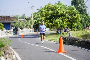 Jogja Maratonu 42K 'nın katılımcıları veya koşucuları, Prambanan tapınak köyünün etrafından güzel bir yoldan geçiyorlar. : Yogyakarta, Endonezya - 18 Haziran 2023