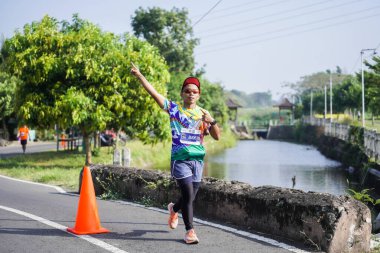 Jogja Maratonu 42K 'nın katılımcıları veya koşucuları, Prambanan tapınak köyünün etrafından güzel bir yoldan geçiyorlar. : Yogyakarta, Endonezya - 18 Haziran 2023