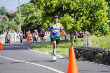 Jogja Maratonu 42K 'nın katılımcıları veya koşucuları, Prambanan tapınak köyünün etrafından güzel bir yoldan geçiyorlar. : Yogyakarta, Endonezya - 18 Haziran 2023