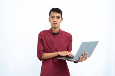 Asyalı bir adam, iş adamı ya da öğrenci konsepti kırmızı günlük kıyafetler giyip minimalist bir dizüstü bilgisayar taşıyor. İzole edilmiş beyaz arkaplan.