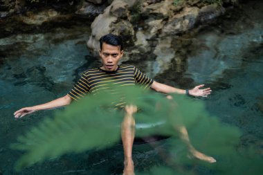 Bir adam yüzen bir tüp kullanarak çok temiz bir bahar nehrinden zevk alır. Udal Gumuk nehri, Magelang, Orta Java, Endonezya.